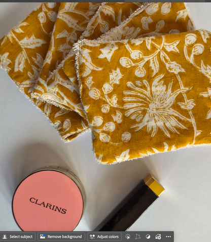  Cosmetic wipesmustard yellow fabric items with a white floral block-print pattern, displayed on a white surface alongside a pink Clarins compact and a black and gold cosmetic tube.